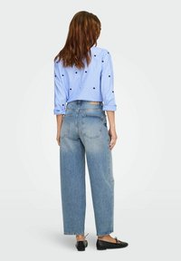 Camisa a rayas azul claro con lunares negros, anudada en la cintura. Combinada con jeans de mezclilla de pierna ancha azul claro de talle alto y zapatos planos negros.