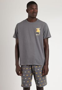 Camiseta de algodón gris de manga corta con un gráfico en el pecho, acompañada de pantalones cortos grises con pequeños patrones amarillos y blancos.