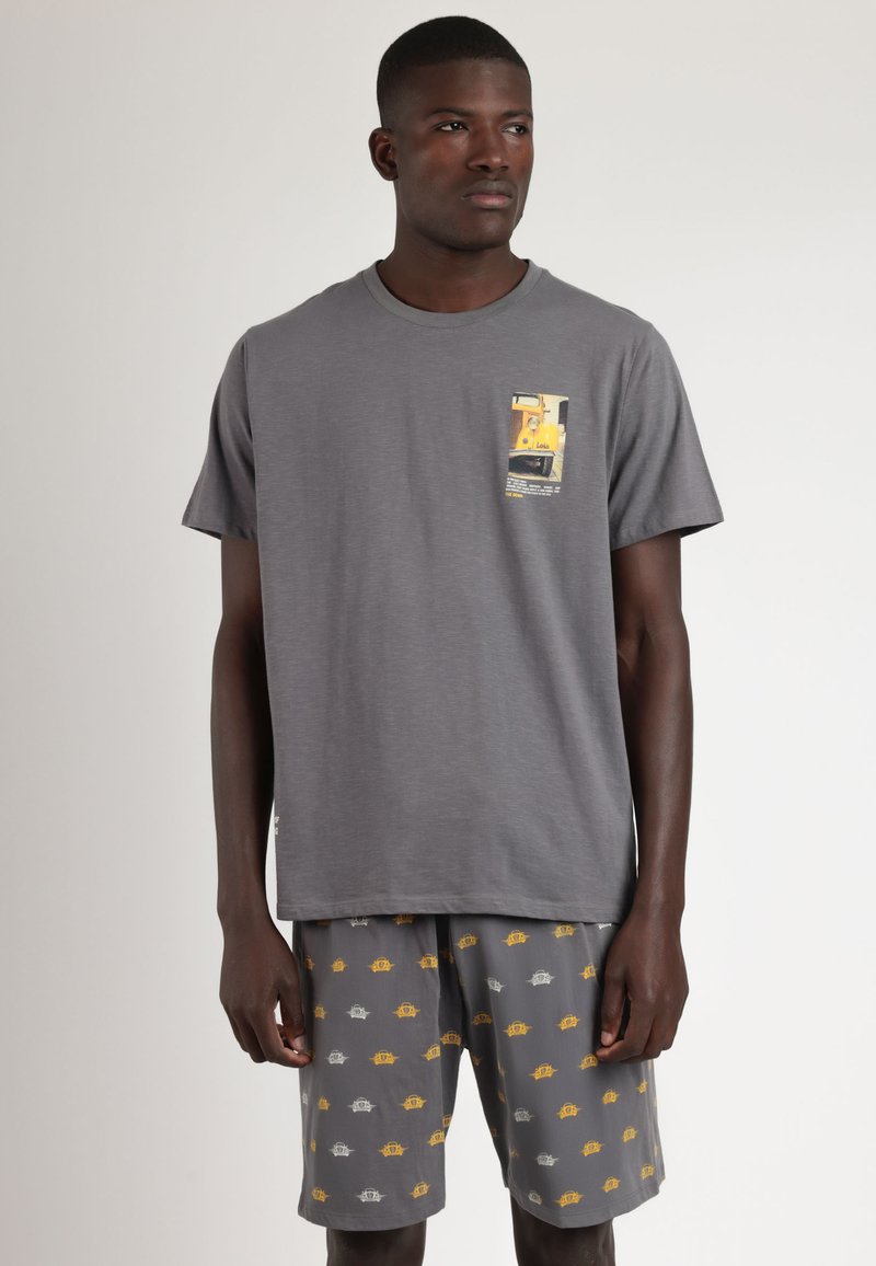 Camiseta de algodón gris de manga corta con un gráfico en el pecho, acompañada de pantalones cortos grises con pequeños patrones amarillos y blancos.