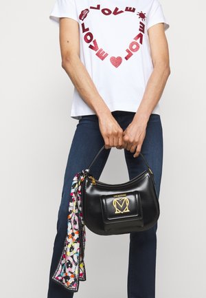 Sorte læder håndtaske med et guld-logo og et dekorativt tørklæde med farverige abstrakte mønstre fastgjort til håndtaget.