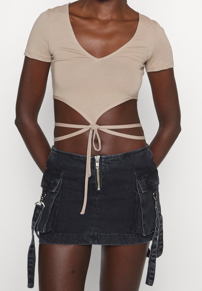 Top corto beige con mangas cortas y escote en V, combinado con una falda mini de mezclilla negra con bolsillos laterales y detalle de cremallera.