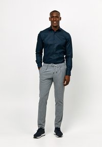 Marine blauwe button-up shirt, getailleerde pasvorm; grijze stoffen broek met trekkoord; zwarte sportschoenen met witte zolen.