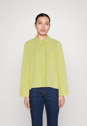 Jasnozielona koszula na guziki z kołnierzykiem, długimi rękawami i kieszenią na piersi, w połączeniu z ciemnoniebieskimi dżinsami. Gładka faktura tkaniny.