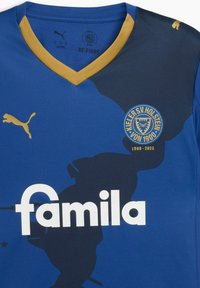 Maglietta da calcio blu con dettagli dorati, a V, con un logo circolare della squadra e la grande scritta bianca "familia" sul davanti.