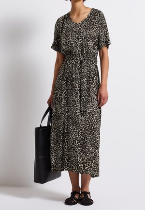 Femme portant une robe midi imprimé léopard à manches courtes, des sandales tissées noires, et tenant un grand sac cabas noir.
