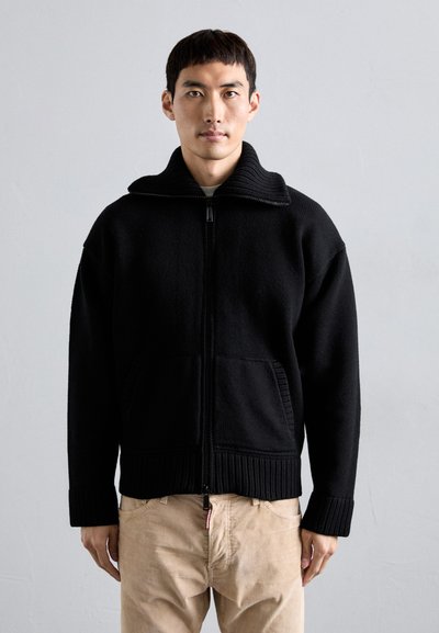 Veste en tricot noir avec un col haut, fermeture éclair sur le devant et poches latérales. Présente des poignets et un ourlet côtelés, un tissu texturé et une coupe décontractée.
