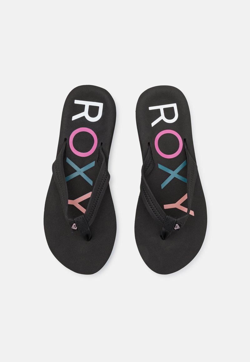 Des tongs noires avec une semelle en caoutchouc et des lanières en tissu, ornées de texte "ROXY" coloré en blanc, rose et teal sur le lit de pied.