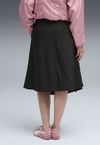 Jupe noire, longueur genou avec un tissu texturé ; portée avec un haut rose à manches longues et froncées et des chaussures de sport rose pâle.