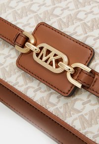 Borsa marrone e crema con esterno decorato, caratterizzata da una chiusura a scatto in metallo dorato e accenti in pelle. Superficie testurizzata con dettagli di cucitura.