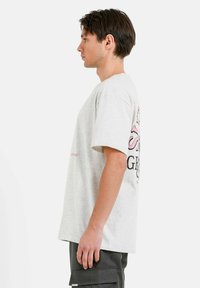 Camiseta de algodón gris con un corte holgado, mangas cortas y un diseño gráfico impreso colorido en la parte posterior, que incluye texto y acentos.