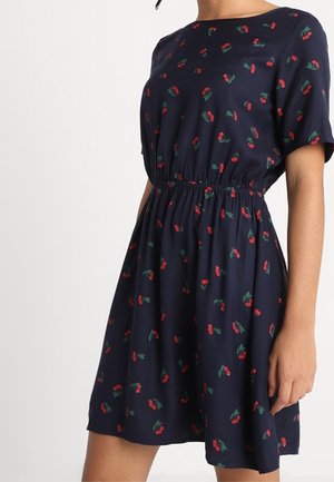 Marineblauwe jurk met korte mouwen, een geplooide taille en een bloemenpatroon van rode kersen en groene bladeren over het geheel. Licht, zacht stof.