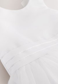 Robe blanche sans manches avec ceinture plissée et détail de tissu doux et fluide pour la jupe.