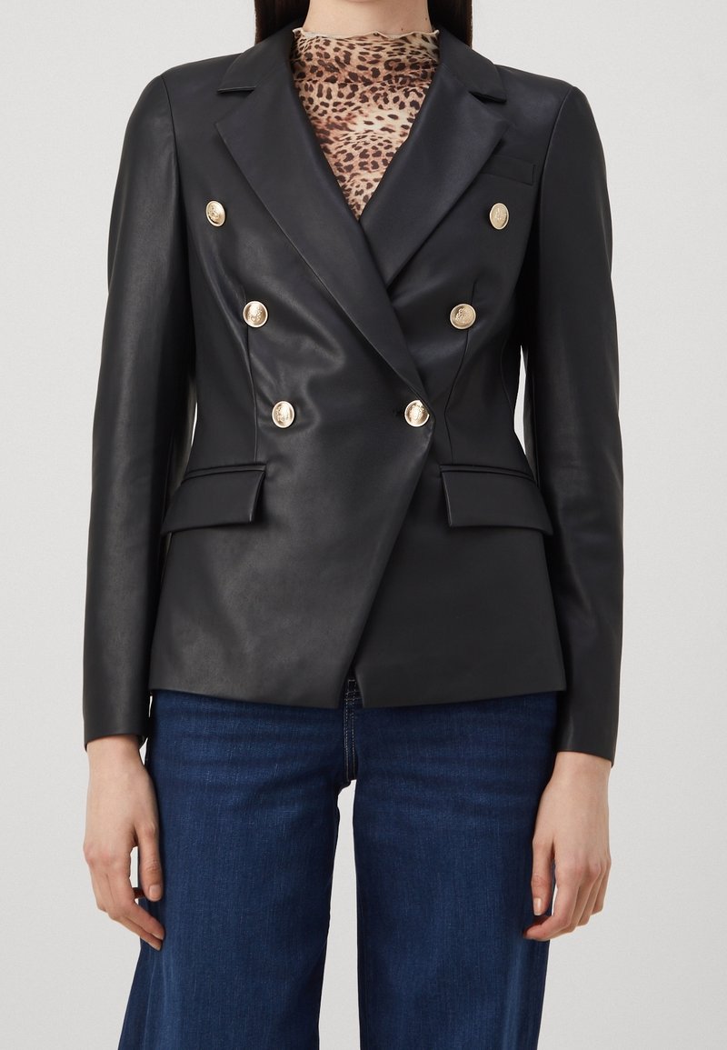 Veste blazer en cuir noir à double boutonnage avec boutons dorés, revers crantés, poches latérales et épaules structurées, portée avec un haut imprimé léopard.