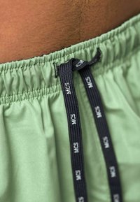 Pantalones cortos verdes con cintura elástica y cordón negro con la marca "MCS", textura suave y tela recogida alrededor de la cintura.