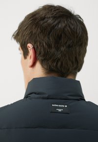 Crna podstavljena jakna s visokim ovratnikom, na leđima s pravokutnom oznakom s ugraviranim "BJÖRN BORG" i "STOCKHOLM 1896".