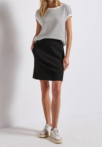 Raidallinen valkoinen ja musta lyhythihainen paita yhdistettynä polvenpituiseen mustaan hameeseen; sisältää sivutaskut ja harmaat lenkkarit.