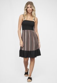 Robe d'été noire à motifs multicolores avec un corsage froncé, un ourlet volanté et des bretelles spaghetti, fabriquée en tissu léger.