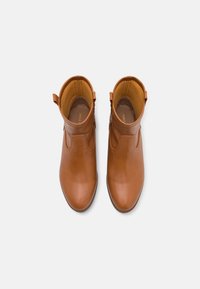 Bottines en cuir marron avec une texture lisse, bout pointu et une fermeture éclair sur le côté. Intérieur doublé en tissu beige, avec un petit talon.