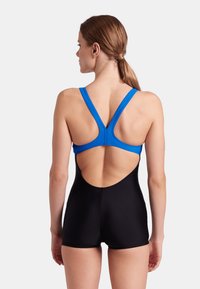 Badeanzug mit einem blauen Oberteil im Racerback-Design und einem schwarzen Unterteil mit kurzen Beinen. Hergestellt aus dehnbarem, glattem Stoff.