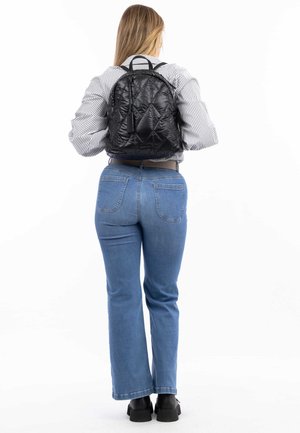 Zaino nero trapuntato con doppi manici superiori, caratterizzato da una texture liscia e un design elegante. Abbinato a jeans blu e scarpe chunky nere.