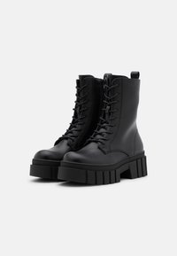 Bottines noires en cuir avec une semelle épaisse, présentant un design à lacets et une languette à l'arrière pour un enfilage facile.