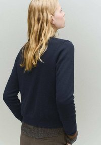 Námornícky modrý sveter s okrúhlym výstrihom a dlhými rukávmi; rebrovaný šedohnedý lem. Hladká textura s priliehavým strihom, pohľad zozadu.
