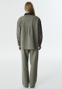 Grijs, textuurshirt en broeken set, met een zwarte kraagdetail. Loose fit, rechte pijpen en een rugplooi op het shirt voor extra stijl.