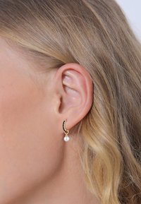 Guldørering med sorte ædelsten og en hvid perledrop, vist på et øre. Glat tekstur og buet design.