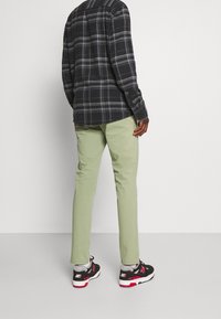Pantalones verdes ajustados, camisa de cuadros en blanco y negro, y zapatillas negras con detalles en rojo y blanco, mostrados desde atrás.