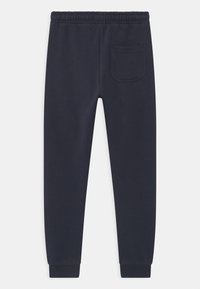 Mörkblå träningsoverallsbyxor i mjukt material med elastiskt midjeband, avsmalnande ben och en bakficka på höger sida. Slät yta.