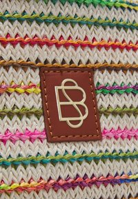 Sac en paille tressée avec des fils colorés entremêlés de rose, vert, bleu et orange. Étiquette en cuir marron avec logo métallique en accent.