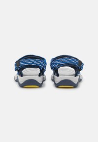 Sandálias desportivas com tiras listradas em azul e branco, palmilha cinza acolchoada e sola preta texturizada com detalhes em amarelo.