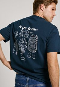Tamno plava pamučna majica s bijelim crtežima prehrambenih artikala i tekstom: "Pepe Jeans® Sunday Roast The Pub London" na stražnjoj strani.