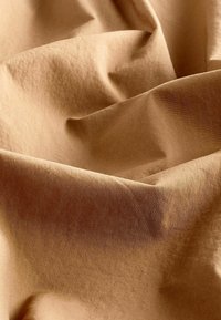 Beige stof, krøllet med en blød tekstur. Overfladen har en let glans og er lavet af letvægtsmateriale, der viser bløde folder.