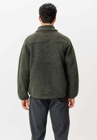 Olivengrøn fleecepullover med høj krave, oversized pasform og tekstureret overflade. Har en sømdetalje i ryggen og løse ærmer.