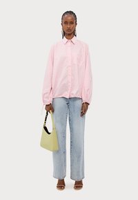 Camisa oversized listrada em rosa e branco com gola abotoada, combinada com jeans de perna reta em lavagem clara e uma bolsa amarela.