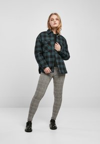 Camicia di flanella a quadri nera e teal con due tasche sul petto, abbinata a leggings grigi a quadri e scarpe nere con lacci.