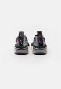 Baskets en mesh noir et vert avec des accents roses, semelles en caoutchouc transparent et languettes de talon noires affichant « MOSCHINO » en lettres blanches.