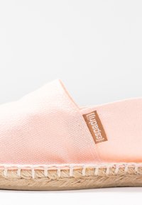 Light pink espadrille made of canvas with a stitched jute sole. Features a side tag with the brand name and a smooth, soft texture.