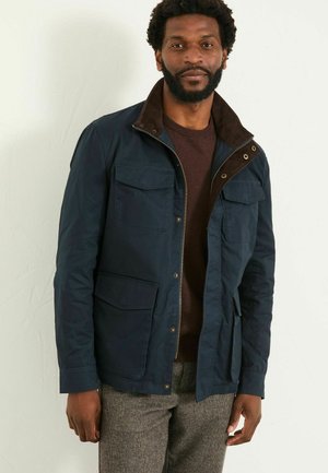 Marineblaue Jacke mit Cordkragen, Reißverschluss vorne und vier Taschen. Glatte Textur, taillierte Passform und Knopfakzente am Kragen.