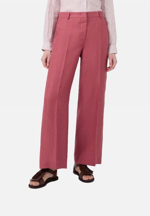 Persona che indossa pantaloni larghi di colore rosa, camicia a righe a maniche lunghe e sandali aperti di colore marrone scuro con nappine.