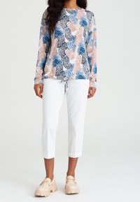 Maglia a maniche lunghe con un motivo astratto multicolore in blu, pesca e nero, abbinata a pantaloni bianchi cropped e scarpe loafers con zeppa color crema.