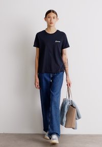 Marinblå bomulls-T-shirt med korta ärmar och en liten logotyp, matchad med ljusblå raka jeans och sneakers. Bär en beige tote-väska.