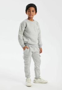 Grå sweatshirt och joggers med en avslappnad passform, tillverkade av mjukt material. Funktioner inkluderar fickor på byxorna och ribbade muddar. Vita sneakers.