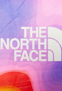 Flerfärgat tyg med en gradient av lila, rosa och röda nyanser, utrustat med stora vita bokstäver "THE NORTH FACE" och en böjd logotypaccent.