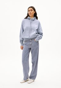 Lichtblauwe hoodie met buidelzak en trekkoordjes, gecombineerd met lichtblauwe hoge taille jeans en witte gevlochten schoenen.