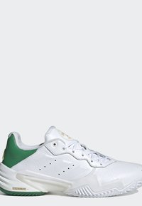 Sneaker in pelle bianca con tallone verde, lacci bianchi, suola texturizzata e design traforato sottile sul lato.