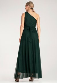 Maxi sukienka w ciemnozielonym kolorze, z jedno-ramiennym krojem, szczegółem w formie kokardy w talii oraz przezroczystą, warstwową spódnicą. Gładka tekstura, elegancki krój.