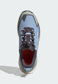 Chaussure de sport bleu clair avec dessus texturé, accents gris, lacets marron et semelle intérieure orange ; équipée d'une semelle rembourrée et d'une languette au talon.