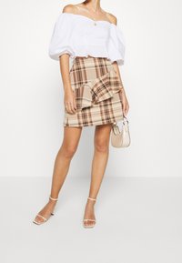 Biała bluzka bez ramiączek z bufiastymi rękawami w połączeniu z beżową spódnicą w kratę z falbaną, dopełniona małą beżową torebką.